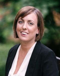 Vicci wearing a white blouse, black jacket, smiling at the camera